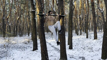 Athletic man doing static exercises on horizontal bar at forest. Sportive guy training abdominal...