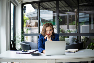 Businesswoman sitting at desk on couch in workplace or at home working on laptop and analyzing data on charts and graphs and writing on papers to make business plan and strategies for company, 