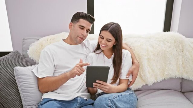 A loving couple relax on a cozy sofa, engaging with a tablet in a modern living room