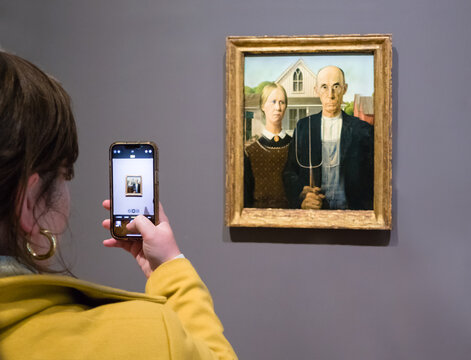 Chicago, Illinois - USA: Looking over the shoulder of a young woman taking a photo on her cell phone of American Gothic 