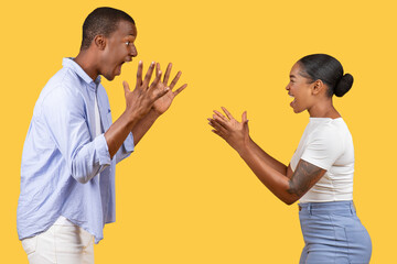 Playful black couple gesturing, surprised expressions, yellow background