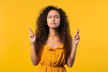 Young woman praying with crossed fingers on yellow background. Guy begs someone