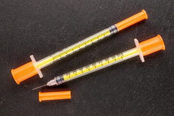 Two medical syringes on slate stone, macro, top view.