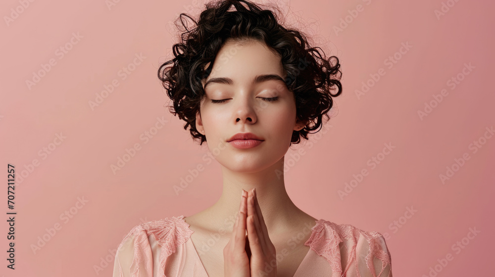 Canvas Prints Young woman with curly hair in a serene pose with her eyes closed and hands together in a gesture of prayer against a soft pink background