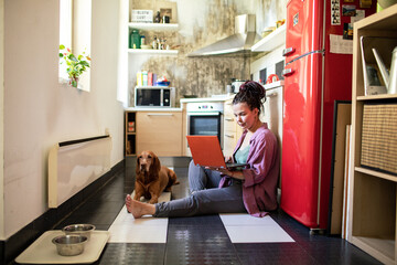 Relaxed woman with dog working on laptop in home kitchen