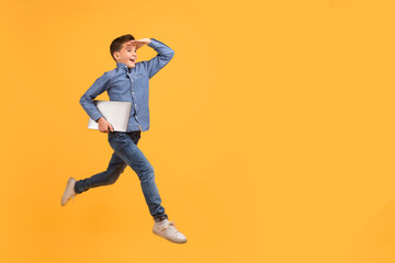 Fototapeta na wymiar Teen boy holding laptop while running on yellow background