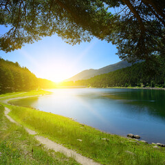 Beautiful sunrise over blue lake and mountains covered with forest.