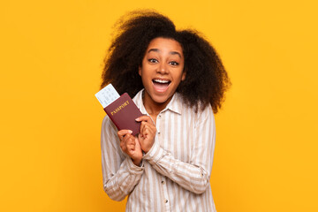 Joyful black woman with passport and boarding pass on yellow backdrop