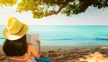 Women sit and reading a book under the tree at seaside. Back view of sexy Asian woman with straw...