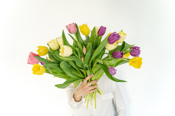 Happy woman holding bouquet of colorful tulips against white wall. Celebration postcard with flowers. Womans day background