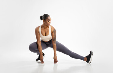 black lady making extended leg squat pose stretching legs, studio