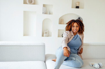 African american millennial girl, contented and happy, sit on comfortable sofa in cozy modern light living room