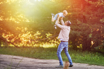 A happy father throws his son into the air in nature. The kid laughs merrily. A father walks with his son in the park.