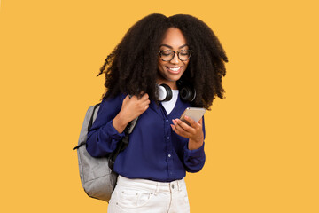 Obraz premium Content black lady student with smartphone and headphones on yellow background