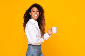 Happy African American woman holding coffee mug on yellow background