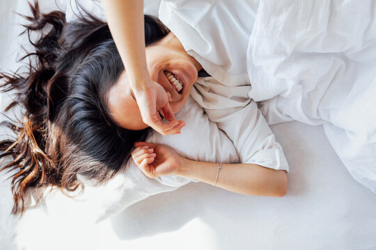 Attractive happy Asian woman lies on a white linen bed in the morning
