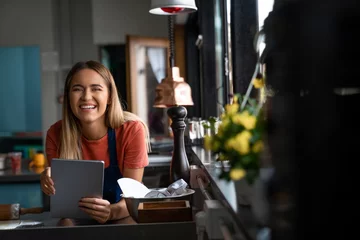 Gordijnen Lovely smiling blonde woman with digital tablet looking at camera in restaurant kitchen. © Dorde