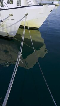 A moored ship rocks on the waves. Reflection in the water of the port at the pier. Ropes hold the white ship at the pier. Spain. Grao, Castellon