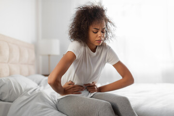 Unhappy black woman touching belly having painful menstrual cramps indoor