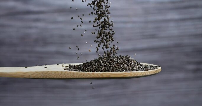 Chia seeds falling into a wooden spoon on gray background. Chia seeds are rich in minerals, omega 3 fat, antioxidants and fiber. Healthy food concept. 4k