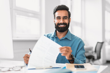 Smiling indian businessman holding paperwork, office setting