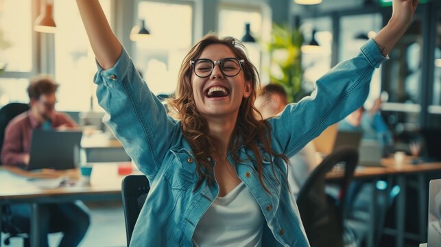 Startup young woman very happy and excited doing winner gesture with arms raised sitting on chair in office.