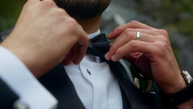 Close-up of the groom standing in front of the waterfall adjusting his bow tie