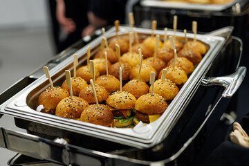 Mini burgers with sesame seeds on a metal tray