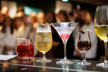 Collection of colorful cocktails on a bar counter with a blurred background of people enjoying their drinks.