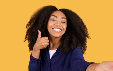 Cheerful black woman giving thumbs up against yellow background