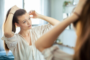 Woman styling her ponytail in the mirror at home