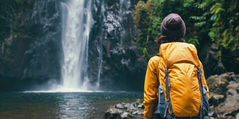 Obraz premium Woman in Yellow Jacket Looking at Waterfall Surrounded by Tropical Greenery