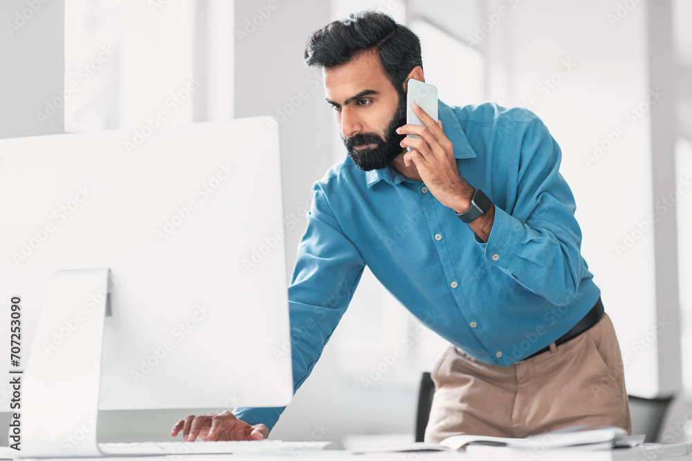 Aufkleber focused indian man multitasking with phone and computer at desk