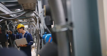 Fotobehang engineer using laptop checking industry cooling air conditioner water cooling tower air chiller of large industrial building to control air system at construction site © HarryKiiM Stock