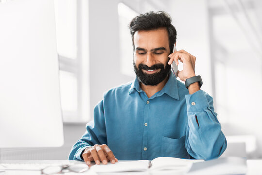 Joyful indian man conversing on phone with planner and glasses