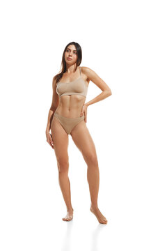 Full-length image of young beautiful woman with slim, fit body standing in underwear against white studio background. Weight-loss. Concept of natural beauty, diet, nutrition, body-positivity