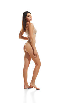 Side view full-length image of young attractive woman with slim, fit, smooth body standing in underwear against white background. Concept of natural beauty, health and body care, weight-loss, sport