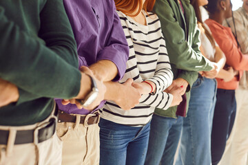 Cropped photo of a group of diverse people students or company employees men and women wearing casual clothes holding hands standing together in a row. Unity, support and team work concept. - Powered by Adobe