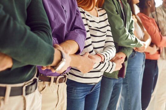 Cropped photo of a group of diverse people students or company employees men and women wearing casual clothes holding hands standing together in a row. Unity, support and team work concept.