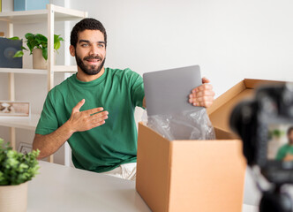 Long stock description: Smiling man in green shirt excitedly unboxing a new silver laptop