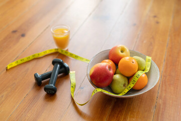 Bowl of fruits, measuring tape, dumbbells and orange juice lying on floor