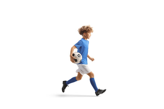 Full length profile shot of a boy in a football kit running with a ball