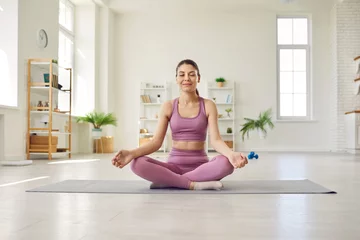 Tischdecke Woman doing yoga at home. Beautiful young girl in sportswear with closed eyes sitting on workout mat in her modern studio apartment, doing lotus pose, meditating, and relaxing © Studio Romantic