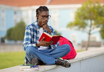 Focused black young man studying reading book sitting outside