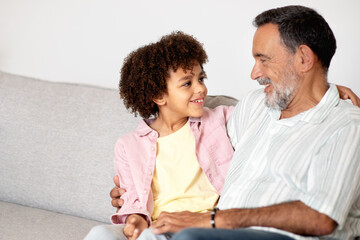 grandfather and grandson sitting on couch hug and talk indoor
