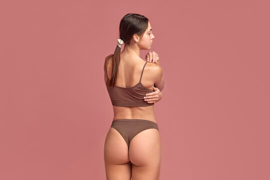 Massage helps to get rid of back pains. Back view image of young girl in underwear holding hands on back, shoulder. Taking care after health and well-being. Concept of beauty, body care, medicine