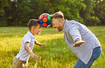Father and son playing with ball in summer. Parent and child having fun in park together. Happy...