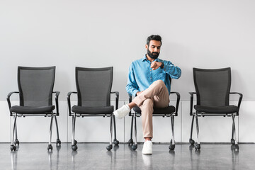 Indian man checking time while waiting in a row of chairs