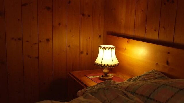 Child turns on bedside lamp inside traditional wooden chalet interior. One little boy turning ON traditional antique light