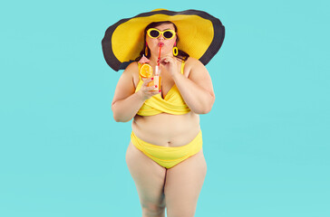 Portrait of fat woman in yellow swimsuit, beach hat and sunglasses drinking orange juice cocktail...